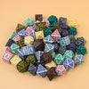 A collection of seven fantasy carved polyhedral dice in various colors and shapes arranged on a light background.