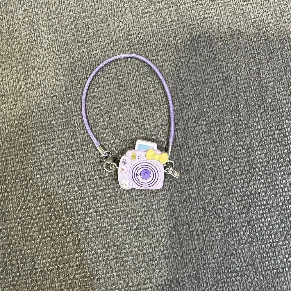 A purple necklace with a small camera pendant and charm for a Labubu doll.
