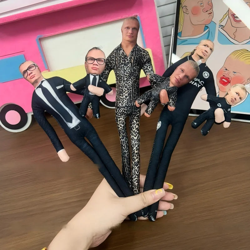 A hand holds a group of Erling Haaland football star stuffed dolls with flexible joints in front of a pink and white backgrou