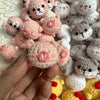 A hand holds a cluster of handcrafted crochet animal keychains including rabbits, chicks, and cats in various pink and gray c
