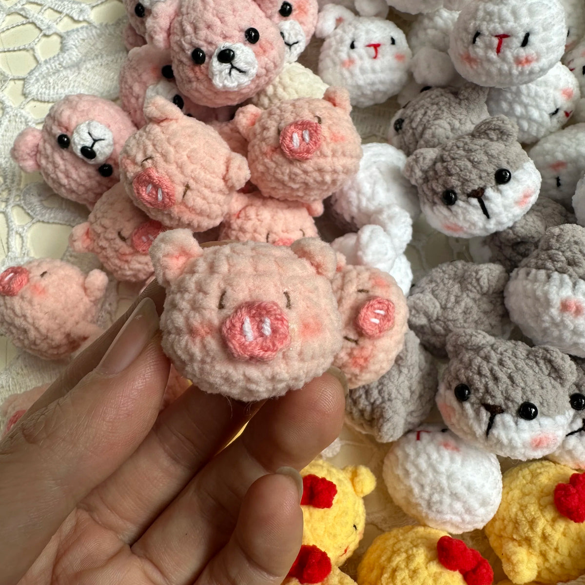 A hand holds a cluster of handcrafted crochet animal keychains including rabbits, chicks, and cats in various pink and gray c