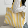 Une personne tient un sac fourre-tout en toile rayée jaune et blanc sur un fond clair.