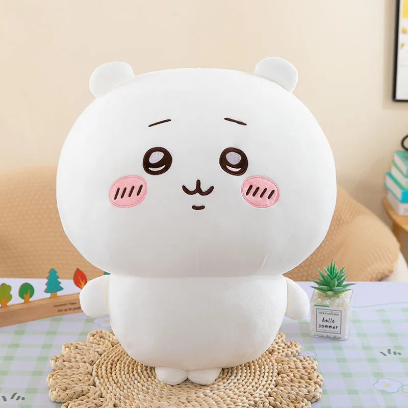 A white Chiikawa plush doll resembling a sleeping animal with pink cheeks sitting on a woven mat.