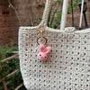 A light beige crocheted bag with a gold-toned keychain featuring a small pink rabbit charm.