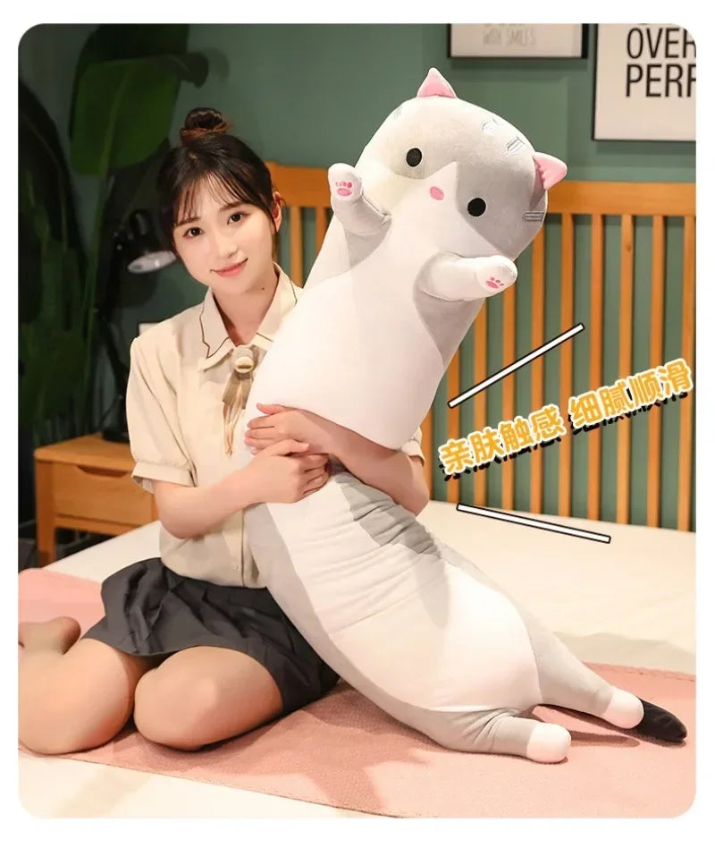 A white plush cat pillow is being held by a young woman in a casual indoor setting.