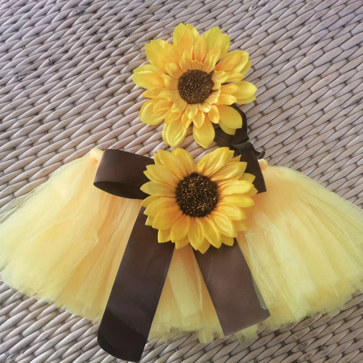 A yellow sunflower baby tutu skirt and headdress set displayed on a woven mat.