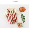 A beige and brown striped baby romper with a bear decoration, paired with a tan hat and light pink shoes.