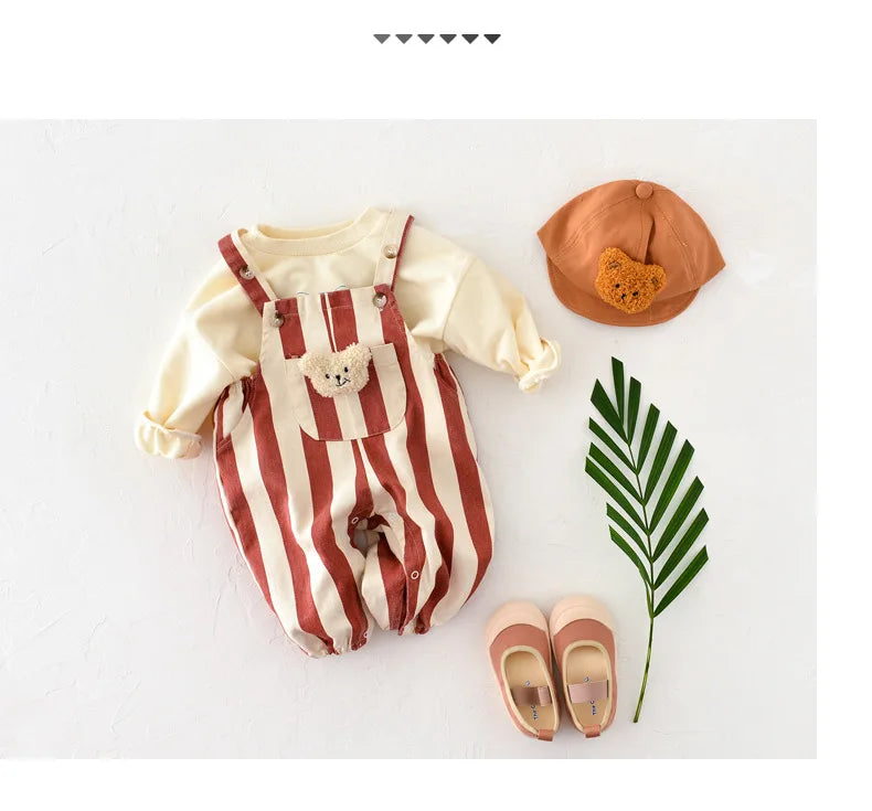 A beige and brown striped baby romper with a bear decoration, paired with a tan hat and light pink shoes.