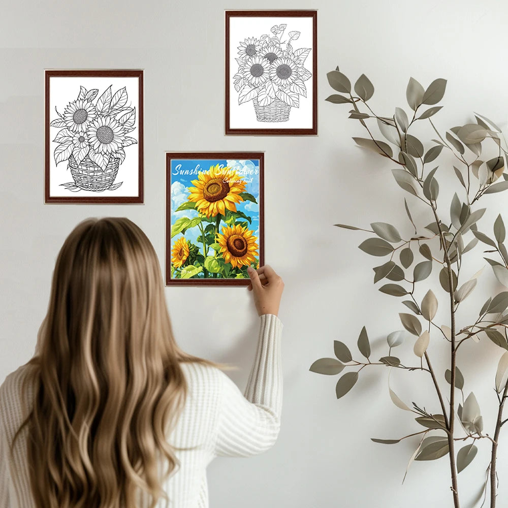 A woman is holding a framed adult coloring book with a sunflower design on a white wall.