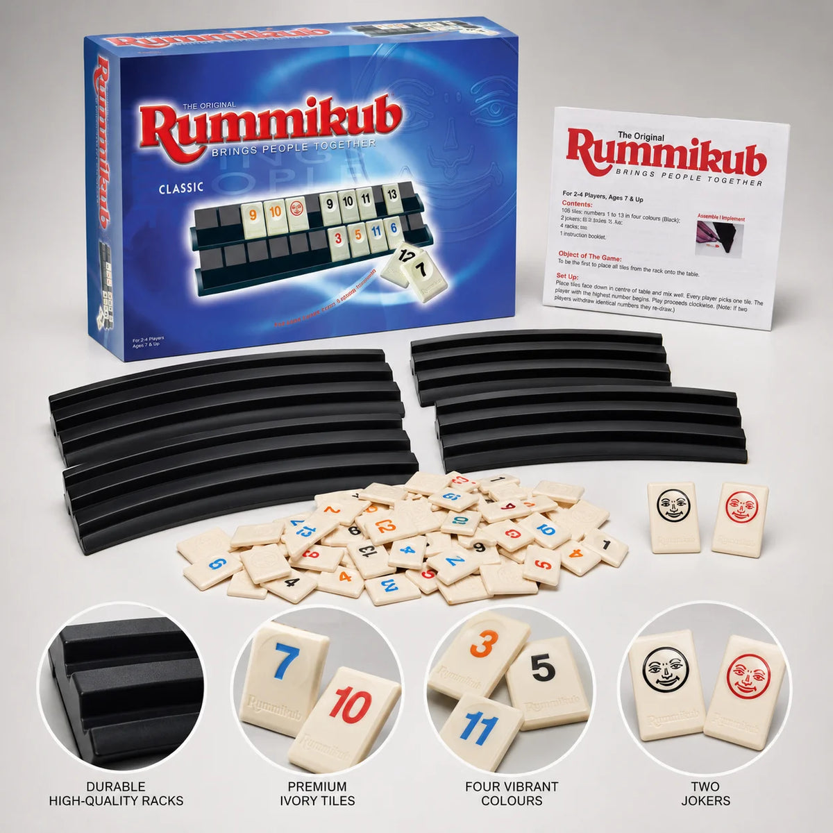 A box of Classic Rummikub tiles and black racks, along with loose ivory tiles and two jokers.