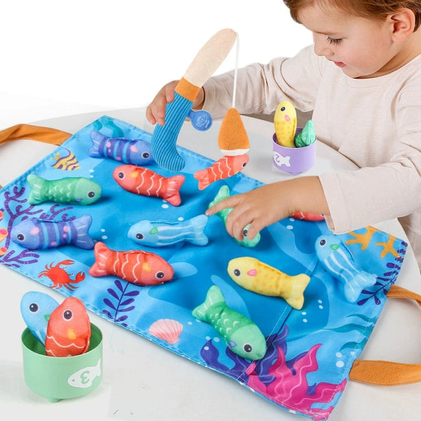 A toddler is playing with a blue cloth fishing game featuring colorful fish and sorting cups for early learning.