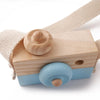 A wooden camera teether toy with a light blue body and natural wood components, attached to a beige fabric strap.
