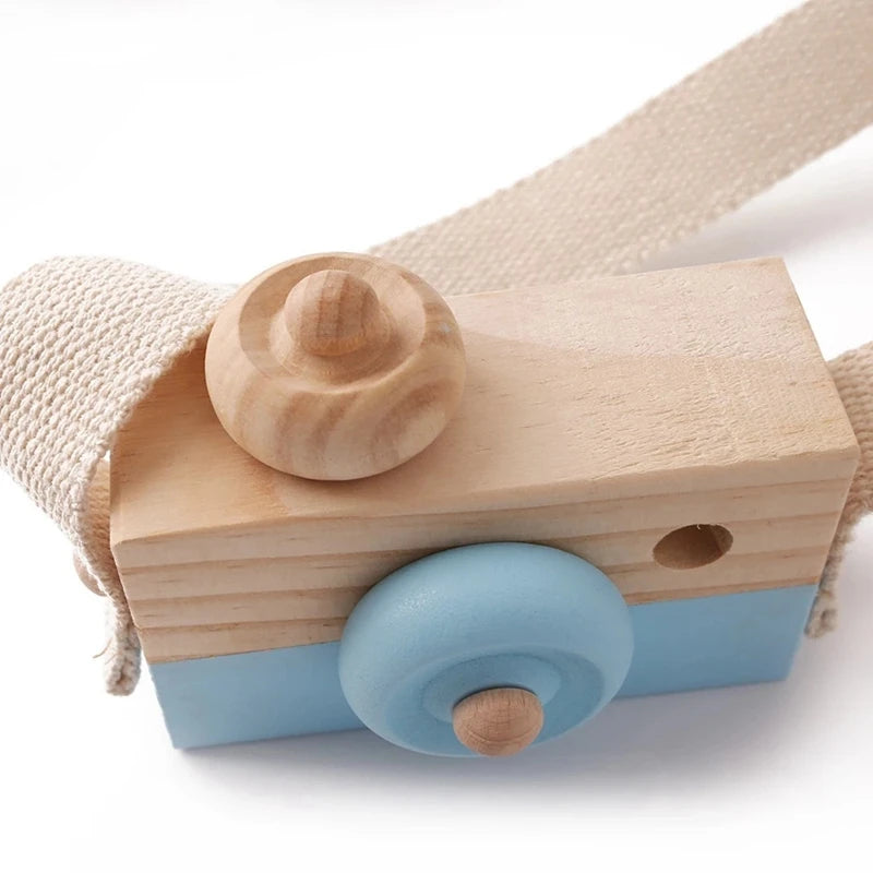 A wooden camera teether toy with a light blue body and natural wood components, attached to a beige fabric strap.