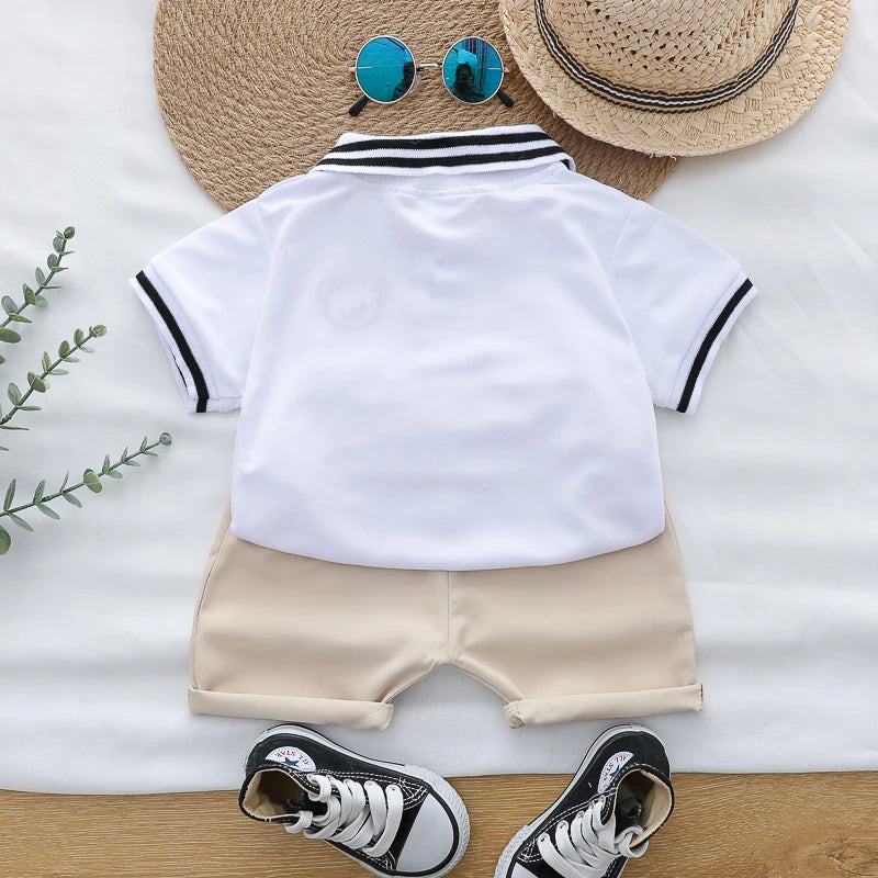 A white polo shirt and beige shorts set for a toddler, displayed with a straw hat and sunglasses.