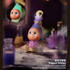 A purple collectible figure with a gold crown and green accents sits next to various glass bottles.