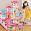 A child stands next to a pink and white miniature castle and villa playset featuring colorful structures and figures.