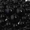 A close-up view of small, round black imitation pearl beads scattered on a white surface.