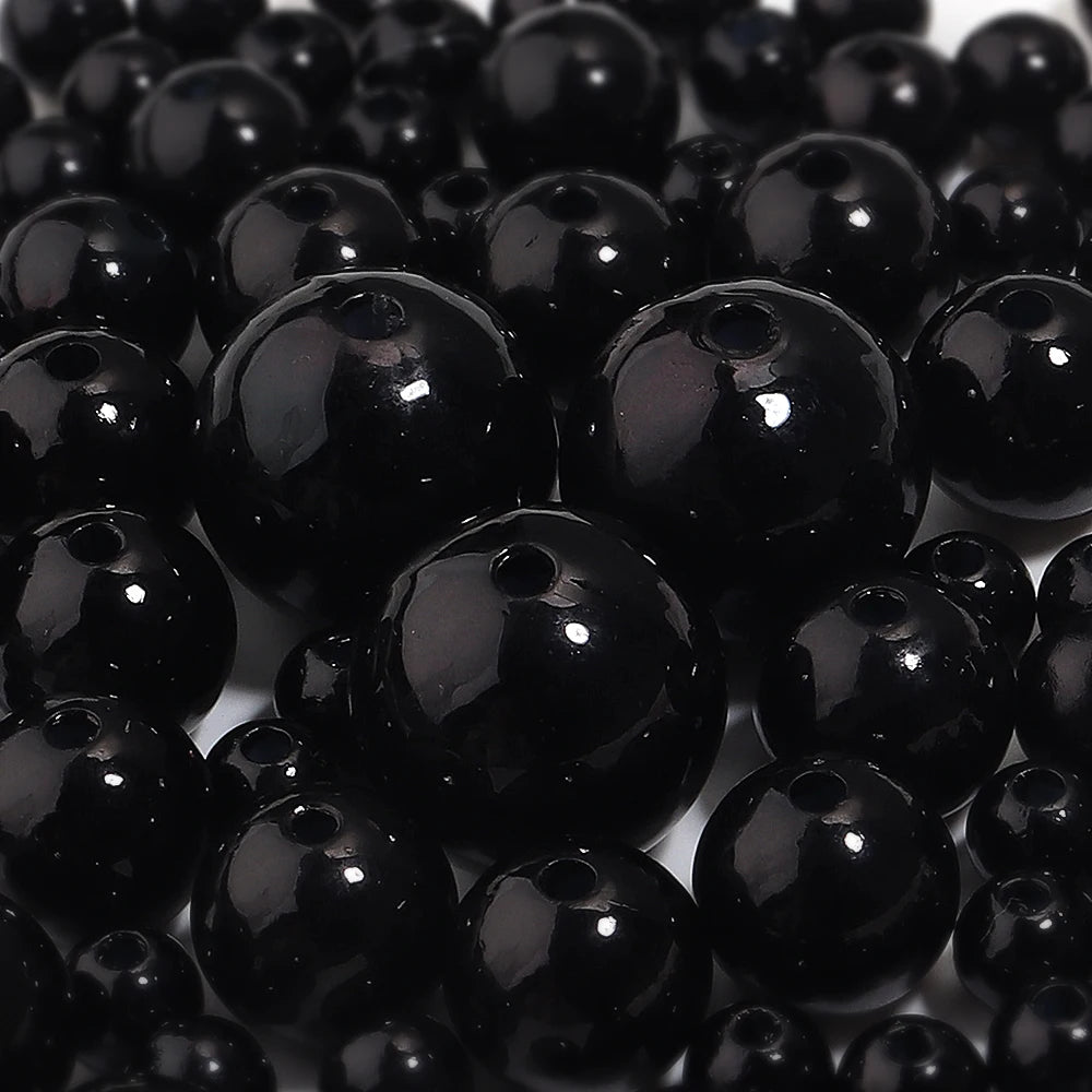 A close-up view of small, round black imitation pearl beads scattered on a white surface.