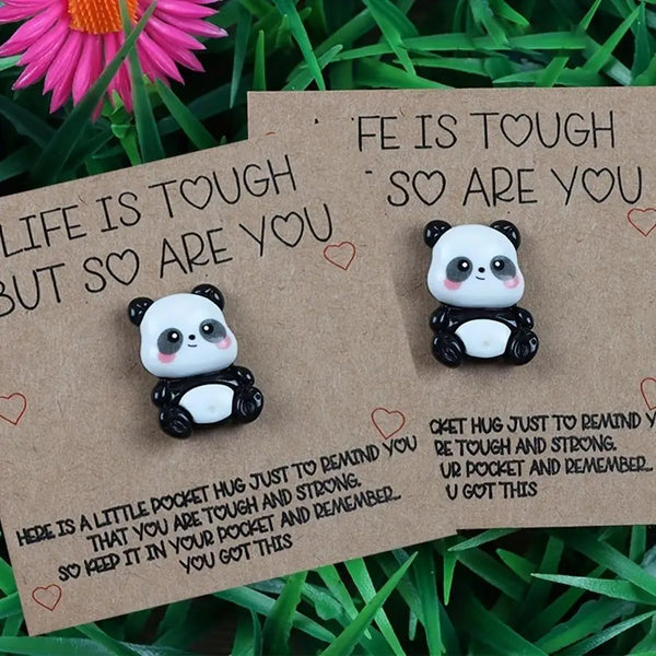 A brown greeting card with text about toughness and a small white panda figure is placed on green grass.