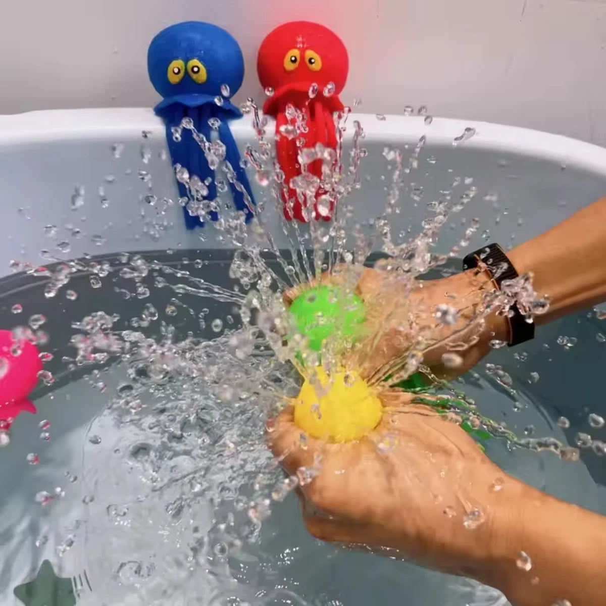 Hands are squeezing a yellow bath toy while water splashes around it in a bathtub with two octopus toys visible.