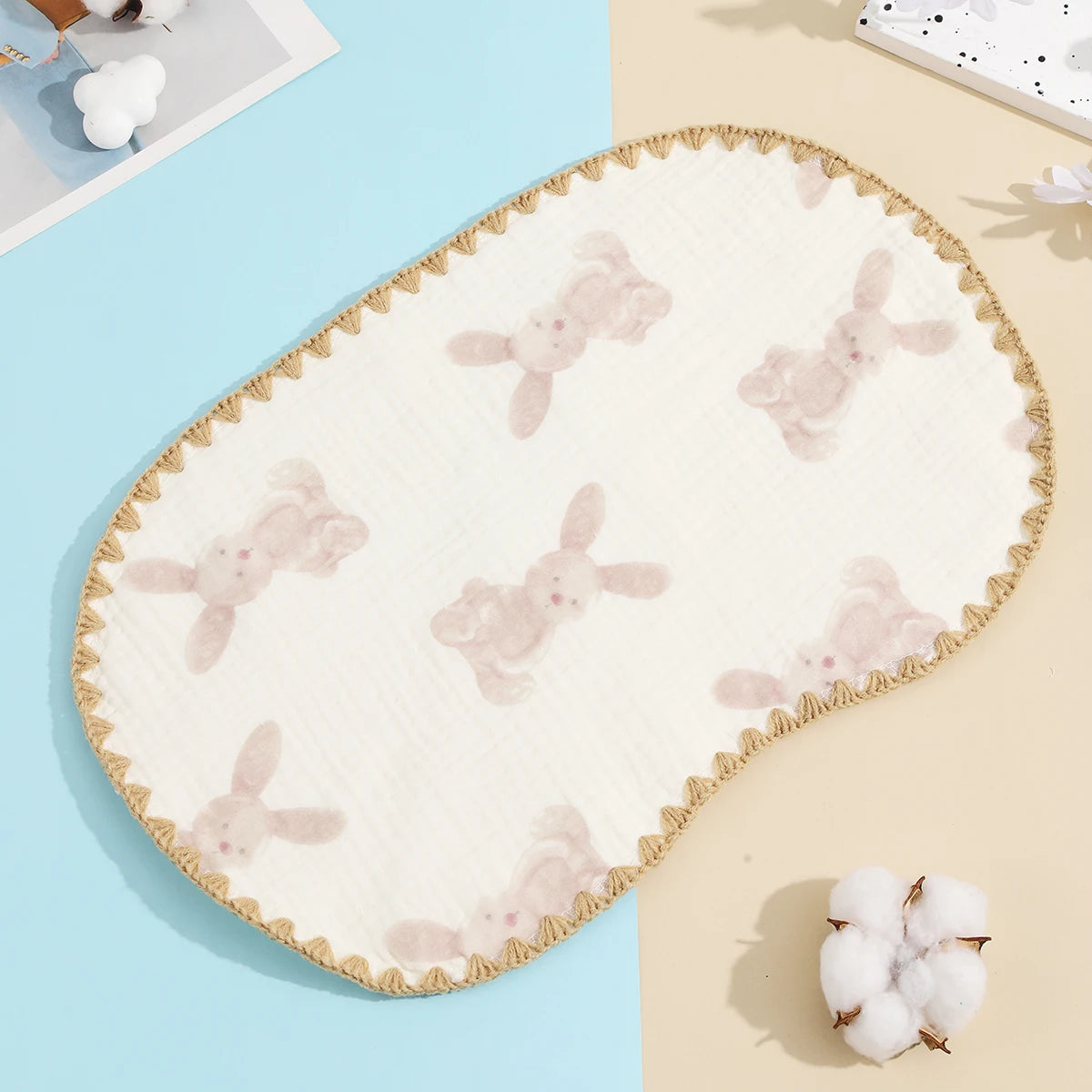 A cream-colored, embroidered flat pillow with a scalloped edge and a light pink bunny pattern on a pale blue background.