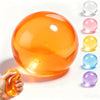 Hand holding an orange coconut oil squishy stress ball with various colored squishies arranged nearby.