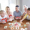 A family playing an animal and nature card game around a wooden table with various cards.