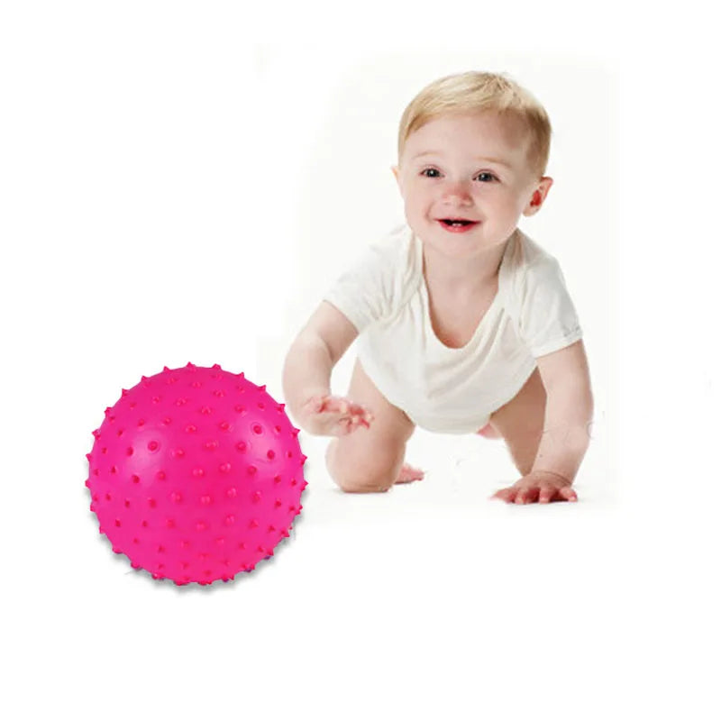 A smiling baby holding a bright pink inflatable sensory ball.