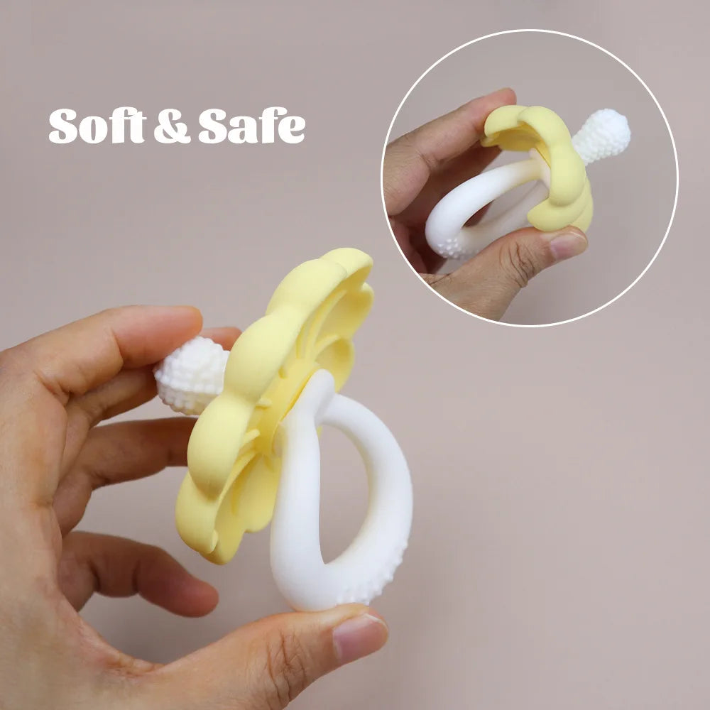 Eine Hand hält eine gelbe Silikonblume und ein Schnuller-Teether für Babys vor einem hellen Hintergrund.