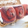 Spools of hand-dyed rainbow merino wool yarn in various shades of red and pink inside a woven basket.