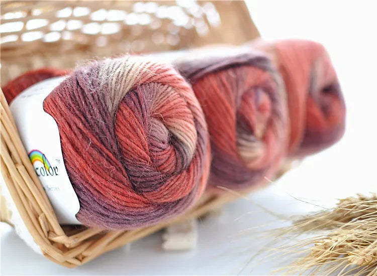 Spools of hand-dyed rainbow merino wool yarn in various shades of red and pink inside a woven basket.