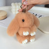 A fluffy, light brown plush bunny keychain with white accents is being held by a hand.