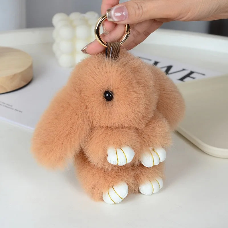 A fluffy, light brown plush bunny keychain with white accents is being held by a hand.