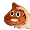 A hand is holding a brown, squishy-looking plush toy shaped like a poop with white facial features.