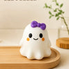 A white squishy ghost stress ball with a purple bow resting on a wooden surface.