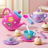 A pink kids tea party playset featuring a kettle, teacup, and cookies on a pink surface.