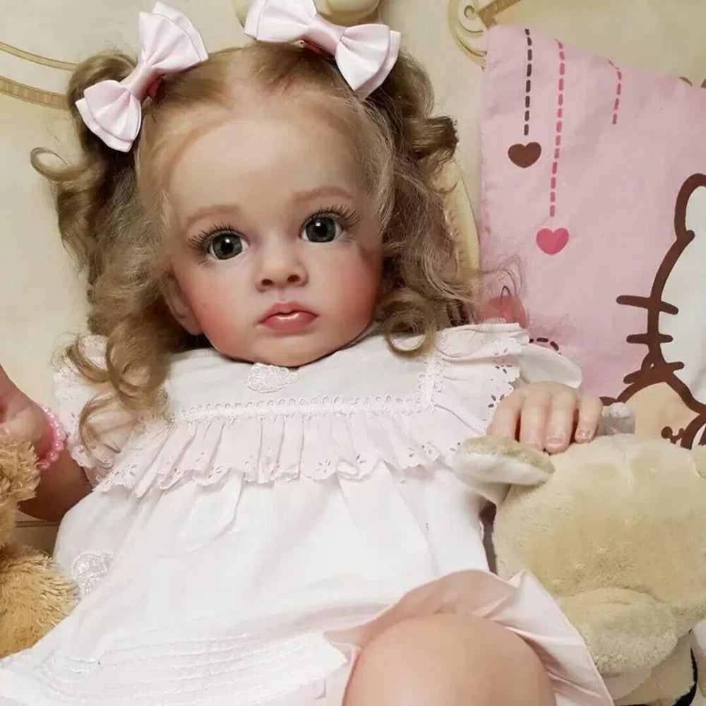 A lifelike reborn baby doll with pink dress and accessories sitting in a light-colored setting.