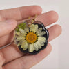 A heart-shaped silicone mold for resin jewelry making featuring a pressed flower design with green leaves and a gold chain.