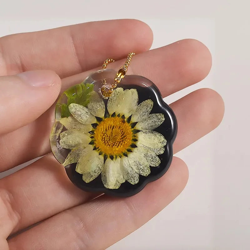 A heart-shaped silicone mold for resin jewelry making featuring a pressed flower design with green leaves and a gold chain.