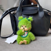 A bright green plush cartoon character with large ears is resting on a gray fabric next to a black handbag.