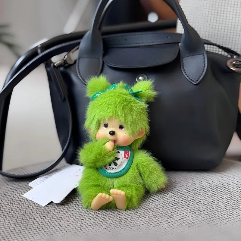 A bright green plush cartoon character with large ears is resting on a gray fabric next to a black handbag.