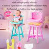 A pink miniature baby doll is shown in a light blue chair with accessories on a purple surface.
