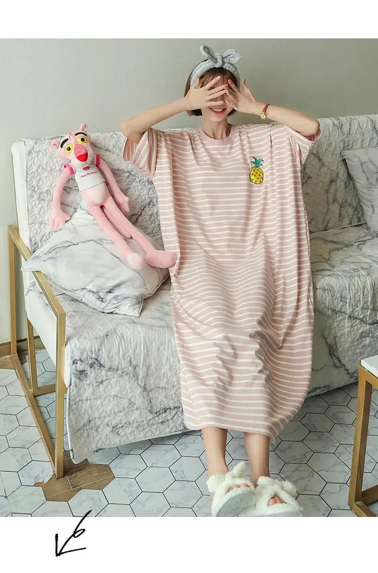 A woman wearing a pink and white striped lounge dress is posing indoors with a stuffed animal.