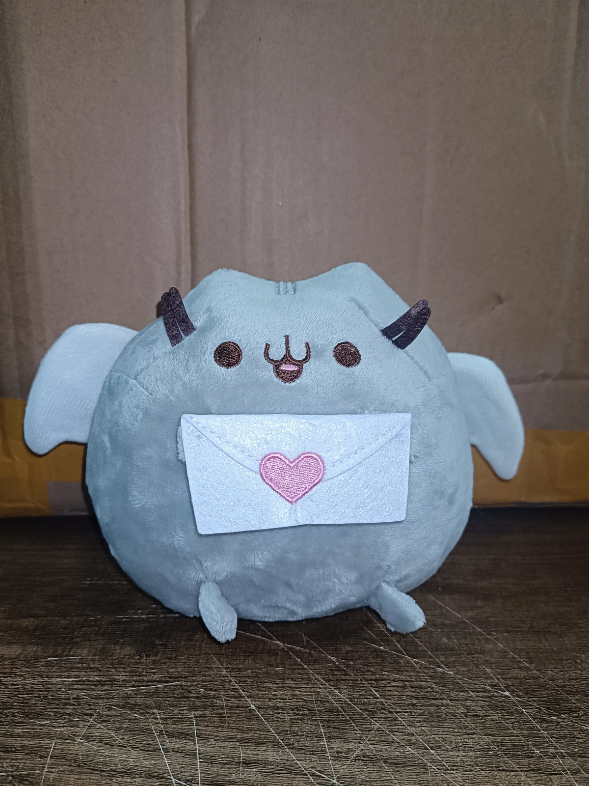 A light blue plush cat doll with horns and a pink heart-shaped envelope on its chest.