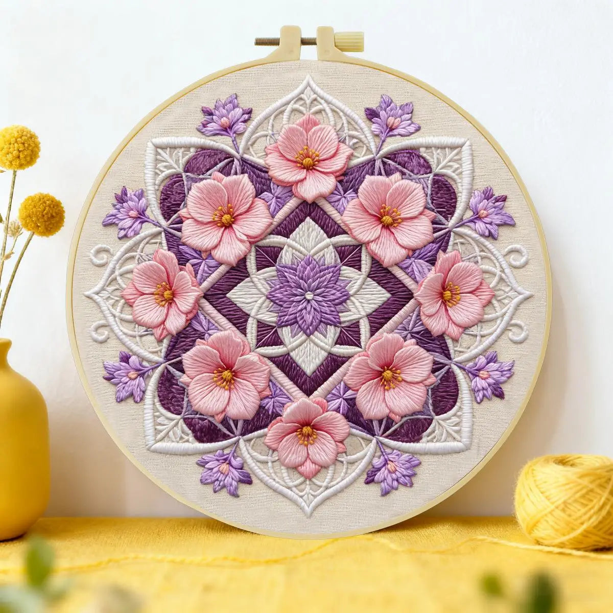 A circular embroidery hoop featuring a detailed floral mandala design in pink, purple, and white thread.