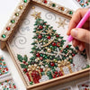 A hand paints a detailed Christmas tree ornament using various colored and pearl beads on a wooden kit board.