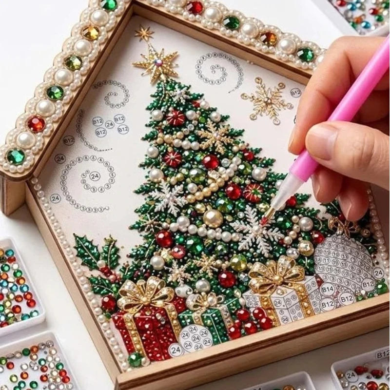 A hand paints a detailed Christmas tree ornament using various colored and pearl beads on a wooden kit board.