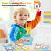 A smiling toddler holds up a learning machine with flash cards and a robot toy in a bright indoor setting.