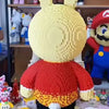 A fully assembled knitted toy resembling a rabbit figure made from yellow and red micro bricks.