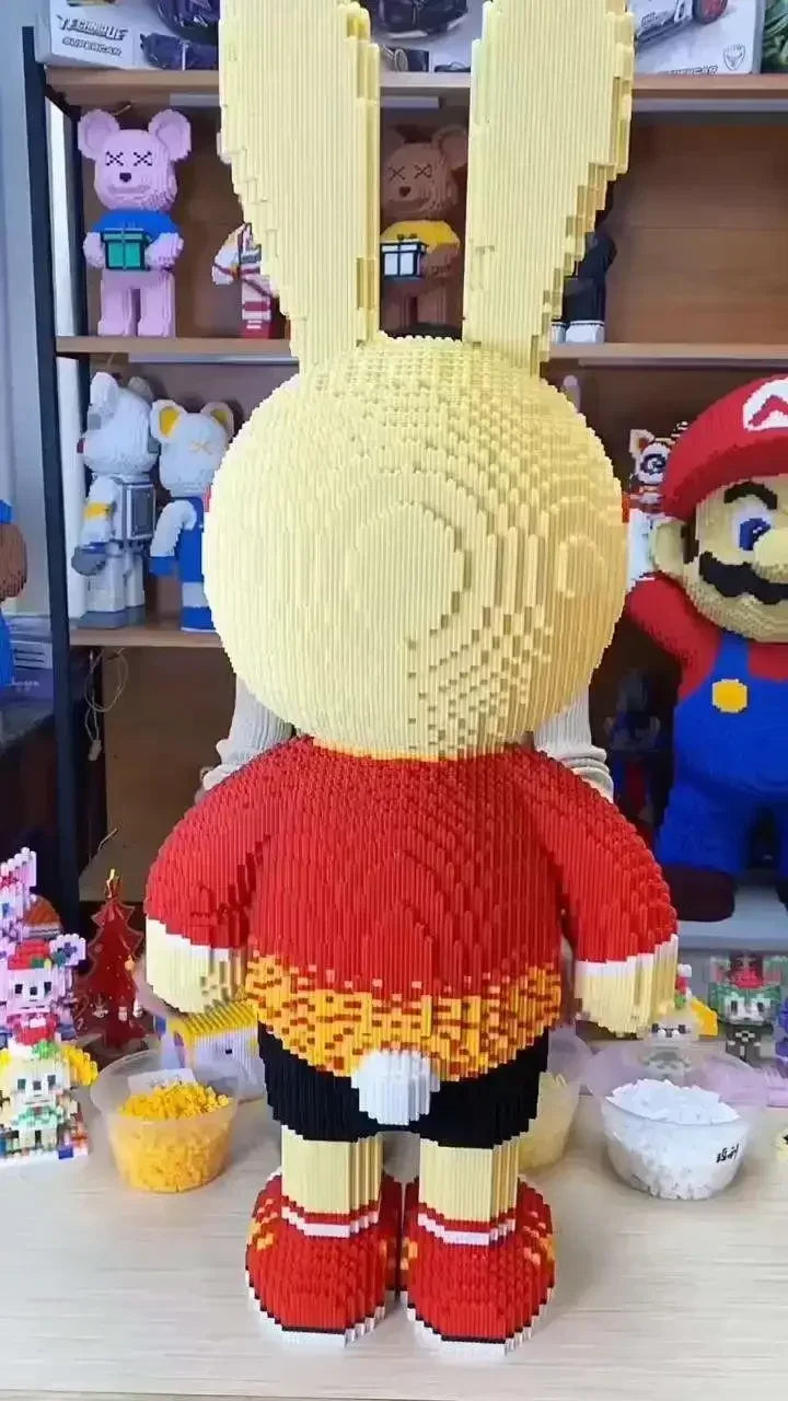 A fully assembled knitted toy resembling a rabbit figure made from yellow and red micro bricks.